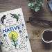 A copy of Native is sitting on a table next to a cup of coffee and an open laptop